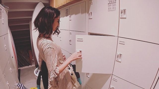 25bcfe59a34d3dd37506308d79bb3937 - SHOP NEWS | ムラサキスポーツオンラインストア 通販 Woman with dark hair in a striped shirt opens a white storage locker in a row of lockers in a laundry room.