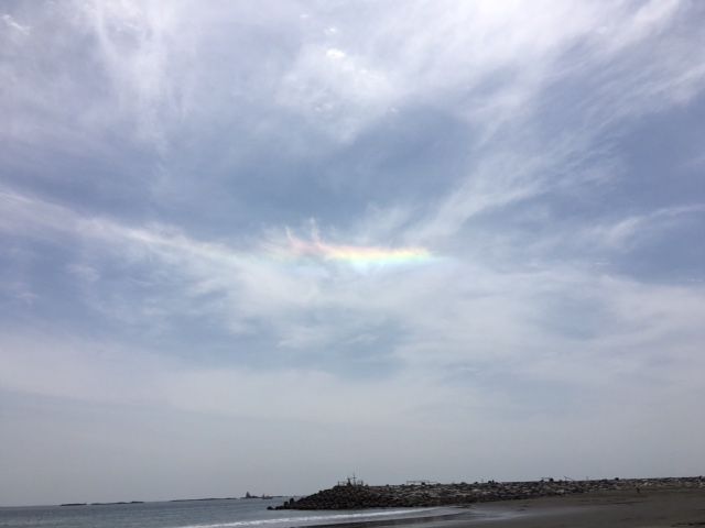 8f425a14ccd3f484dabd69202cbcf0ed - SHOP NEWS | ムラサキスポーツオンラインストア 通販 Sun halo rainbow in a pale blue sky over a calm sea with a rocky breakwater in the distance.