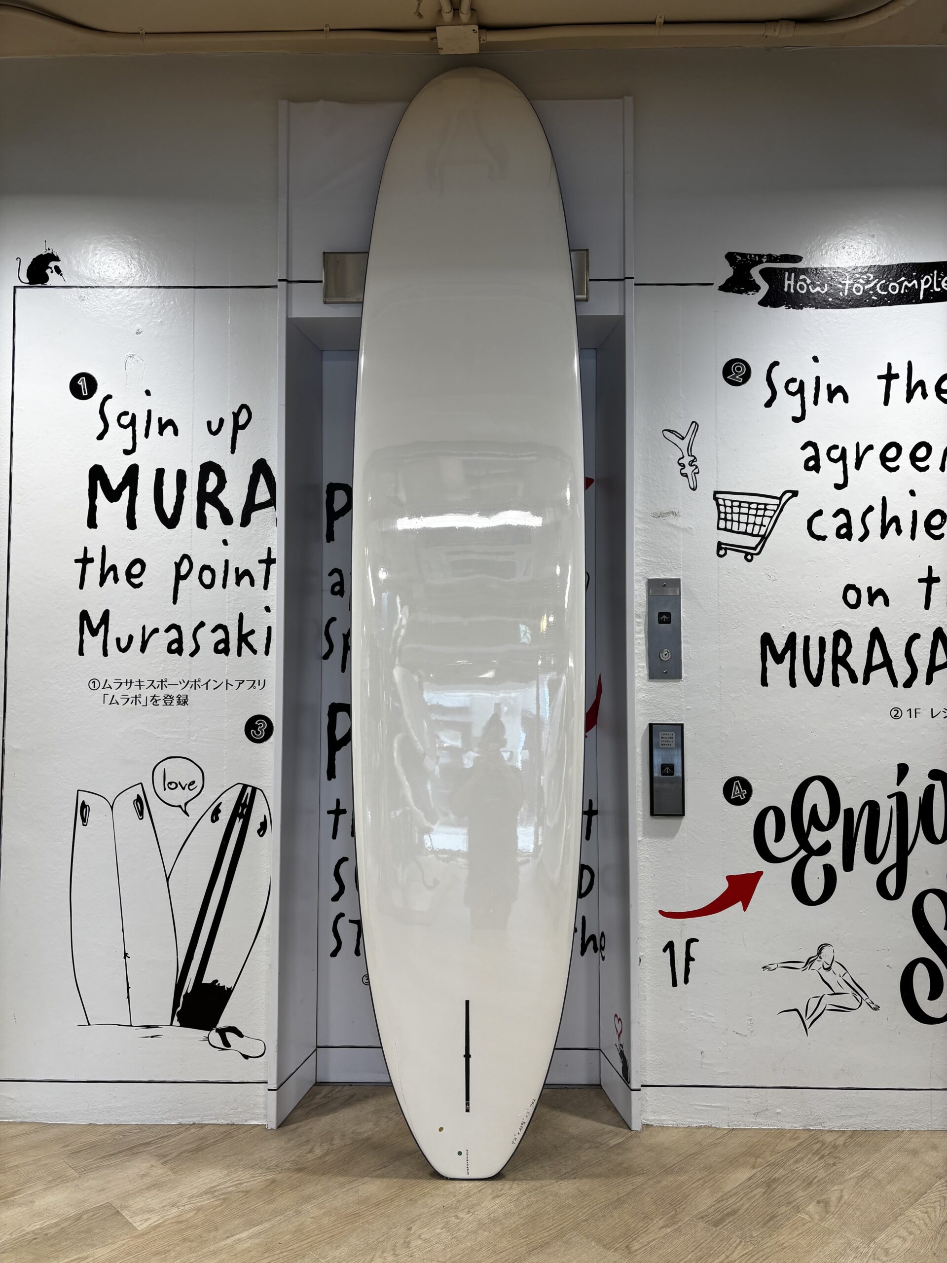 White surfboard standing upright in a wall alcove, surrounded by black handwritten text and drawings on the walls.