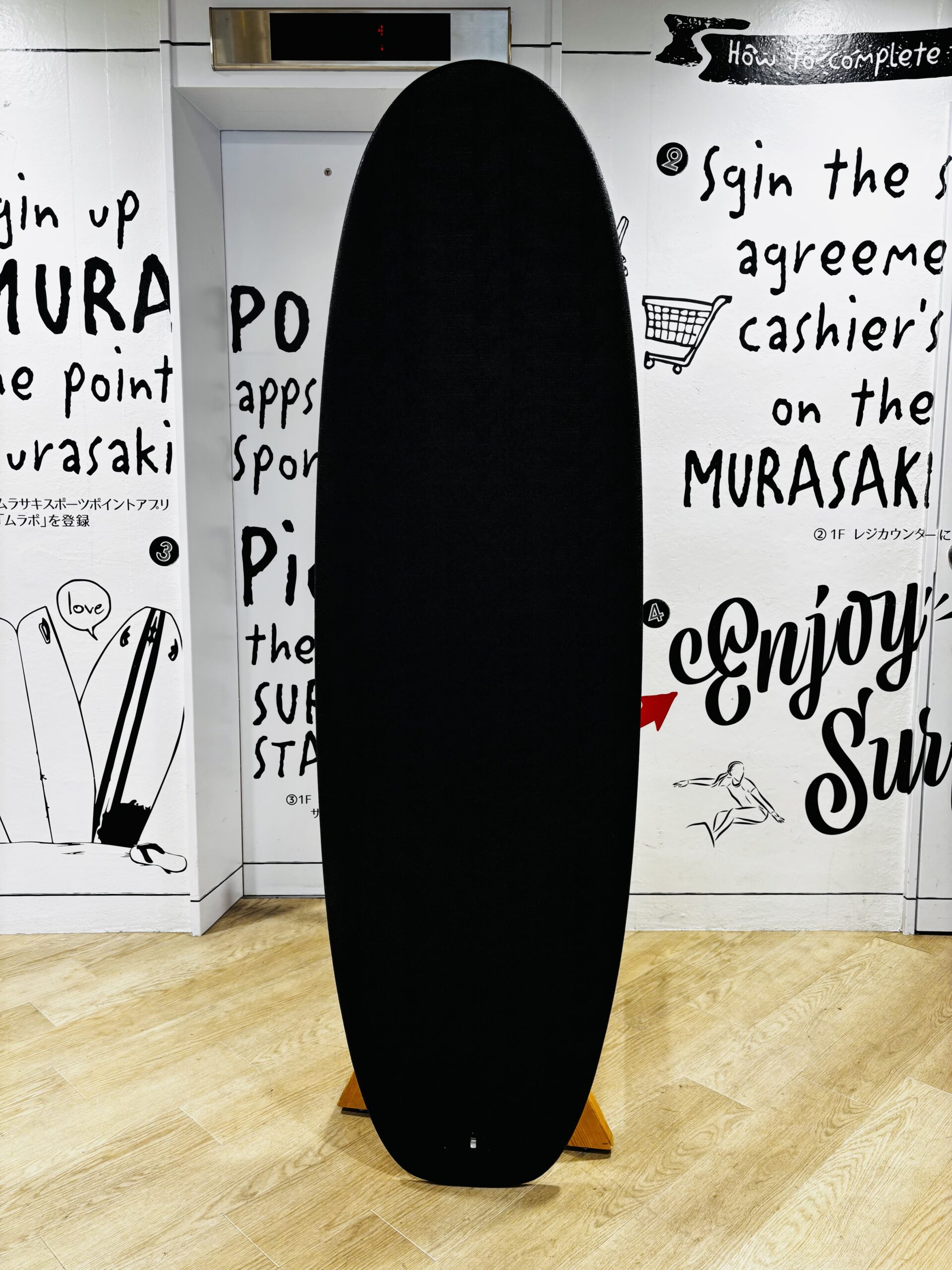 Tall black curved sculpture stands upright in a white gallery with handwritten wall text as background.