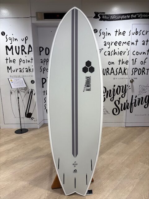 IMG_7078 - SHOP NEWS | ムラサキスポーツオンラインストア 通販 White surfboard with two dark gray stripes on display in a showroom or shop.