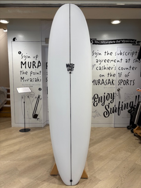 IMG_8828 - SHOP NEWS | ムラサキスポーツオンラインストア 通販 White surfboard on a wooden stand in a shop, featuring a central stringer and small logo in the middle.