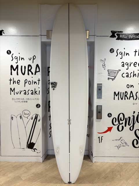 IMG_8852 - SHOP NEWS | ムラサキスポーツオンラインストア 通販 White surfboard standing upright between graffiti-covered walls with handwritten text and drawings.