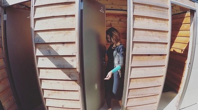 b93aa8bd374dc9966e0832b094d4f56a - SHOP NEWS | ムラサキスポーツオンラインストア 通販 Woman in a denim jacket opens a tall door between wooden storage lockers or sheds.
