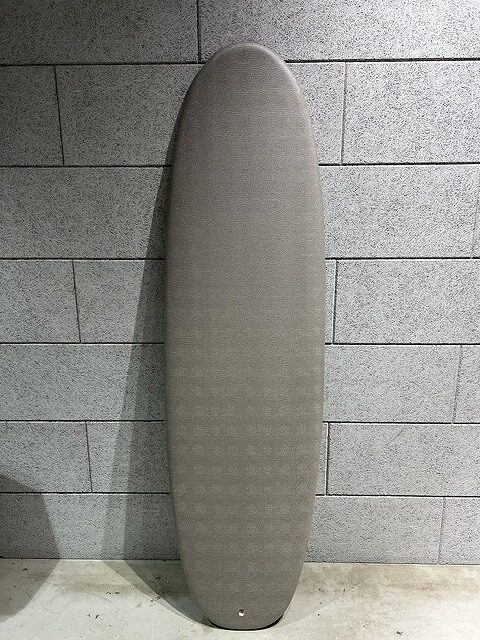 Gray surfboard leaning vertically against a gray tiled wall.