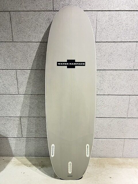 Tall pale gray surfboard leaning against a concrete block wall, featuring a 'Water Rampage' logo and three fin boxes at the bottom wall side edge.