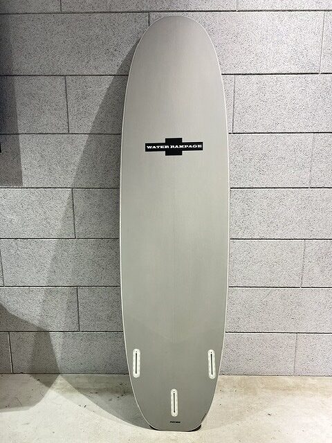 Grey surfboard standing upright against a tiled wall with a small black Water Rampage logo in the center.