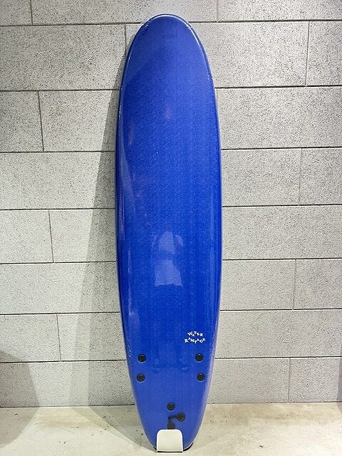 Blue surfboard standing upright against a light gray brick wall inside an indoor space.