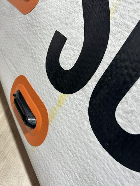 Close-up of a white textured surface with large black letters and an orange circular vent/button near the edge (part of a sign or board).