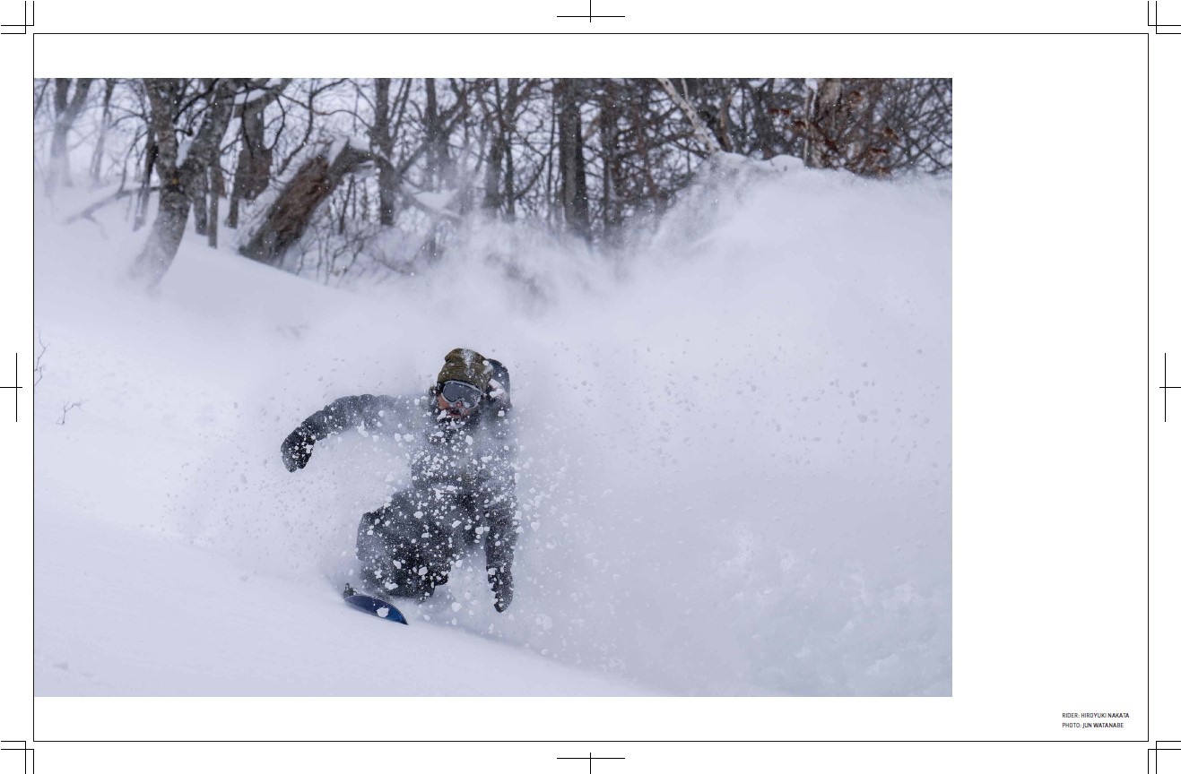 Snowboarder carving through fresh powder with trees in the background.