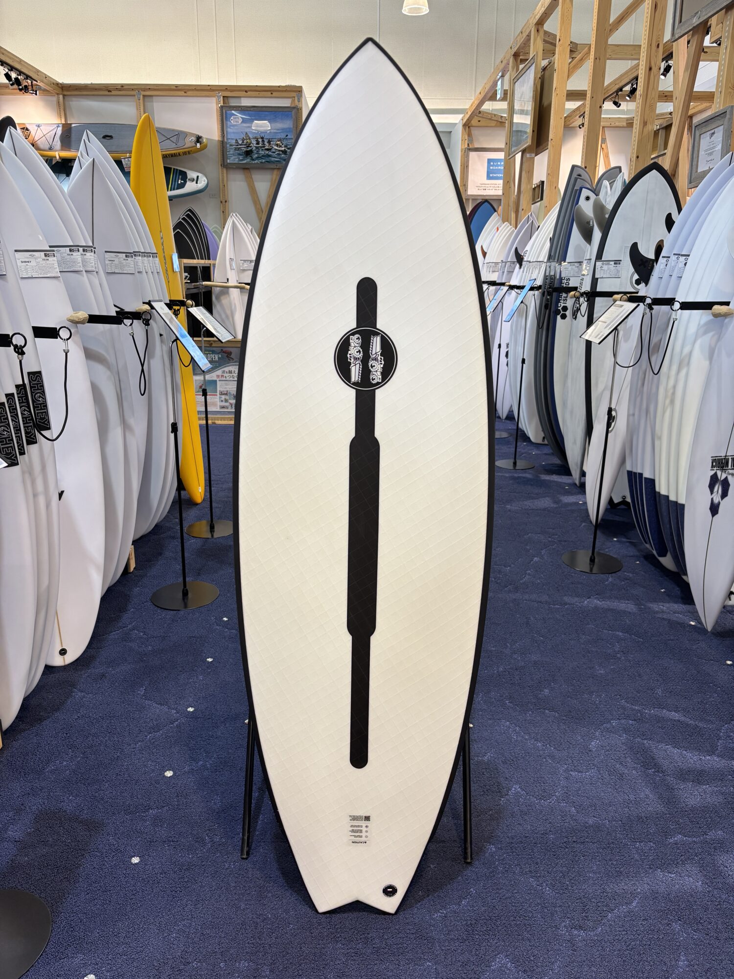 White surfboard with a black center stripe on display among many other boards in a showroom.