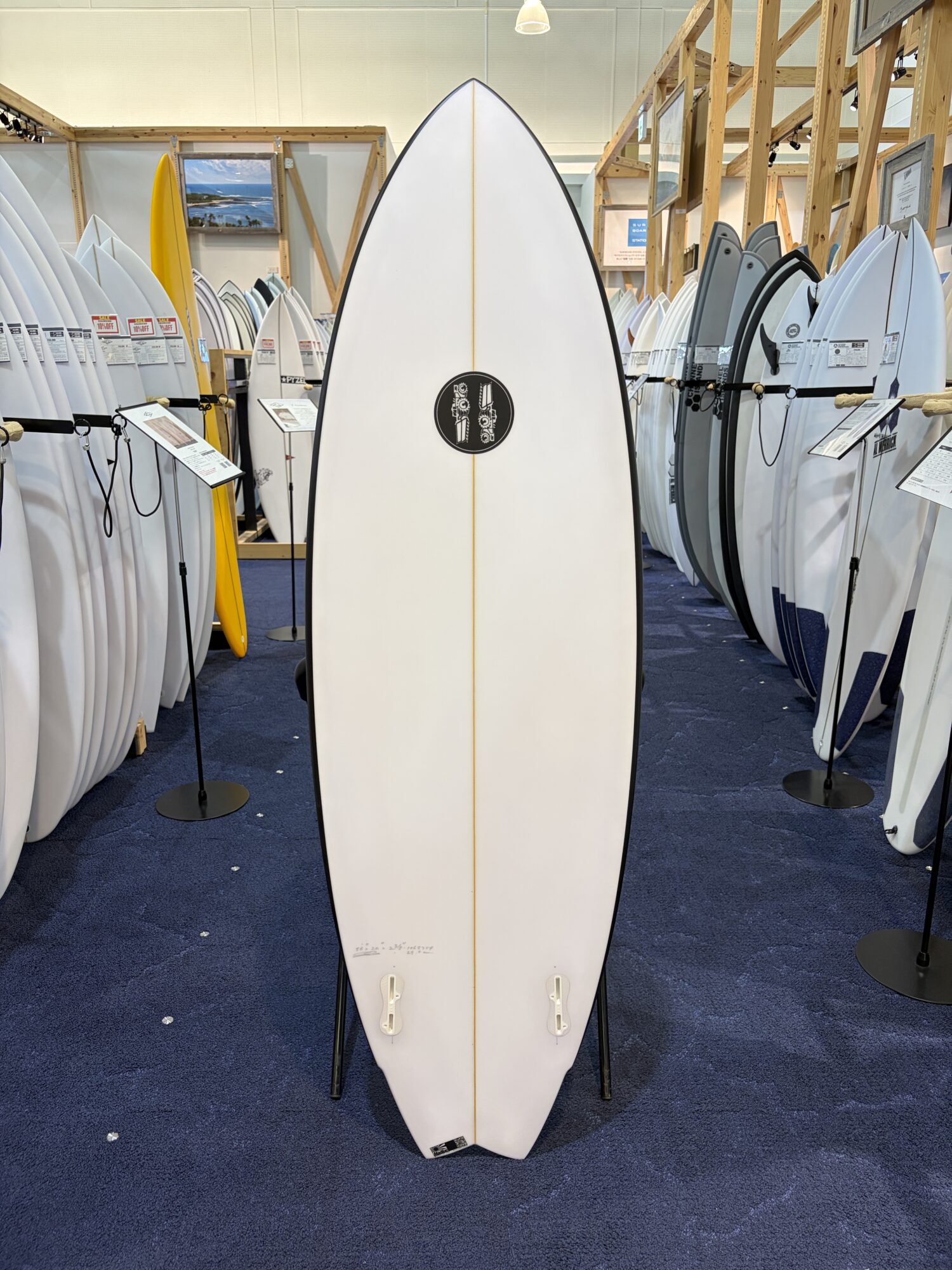 Tall white surfboard standing upright on a display rack, surrounded by other boards in a surf shop showroom.