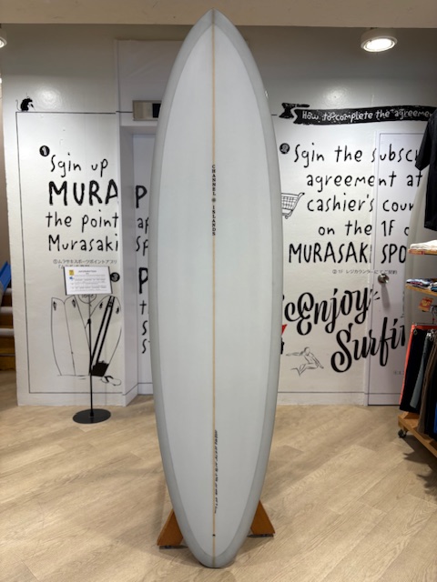 Display surfboard standing upright on a wooden stand in a shop, with graffiti-style wall graphics in the background.
