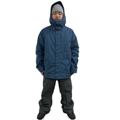 Child wearing a blue winter parka with hood up, gray knit hat, and dark snow pants standing with feet apart.