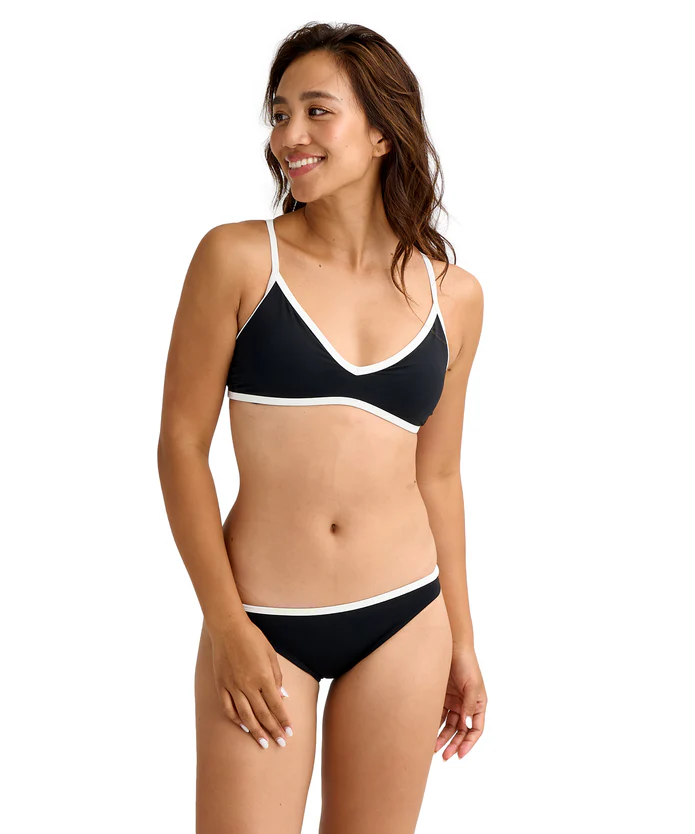Woman smiling, modeling a black bikini with white trim on top and bottom against a white background.