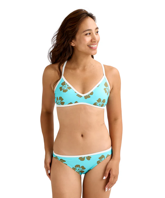 Woman wearing a turquoise hibiscus-print bikini with white trim, smiling and looking to the right.