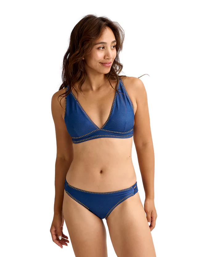 Woman in a blue bikini posing in a studio against a white background, looking to her left.