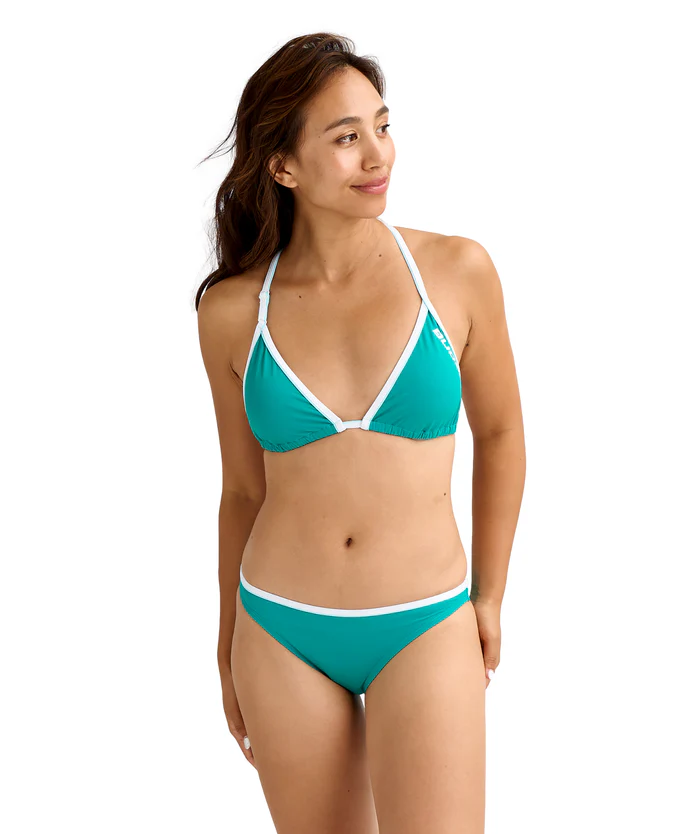 Woman wearing a teal triangle bikini with white trim, standing and looking to the side against a white background.
