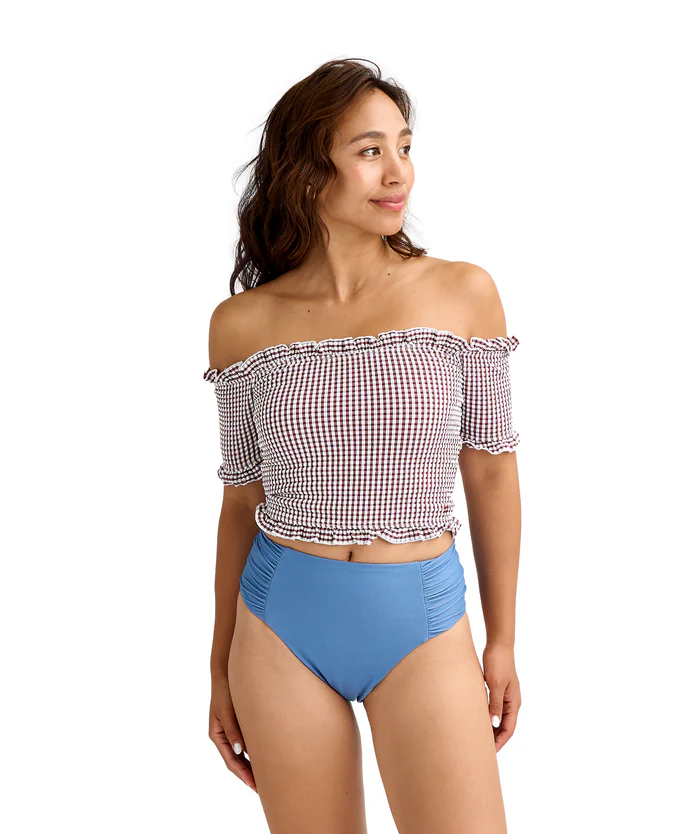 Woman in a red-and-white off-the-shoulder gingham bikini top and blue high-waisted bottoms, looking to the side.