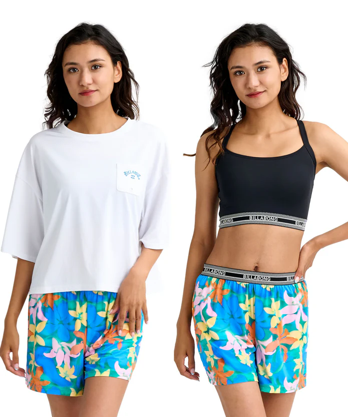 Two models showcase vibrant tropical-print swim shorts; left in a white oversized T-shirt, right in a black sports bra and matching shorts posterized at the hips.