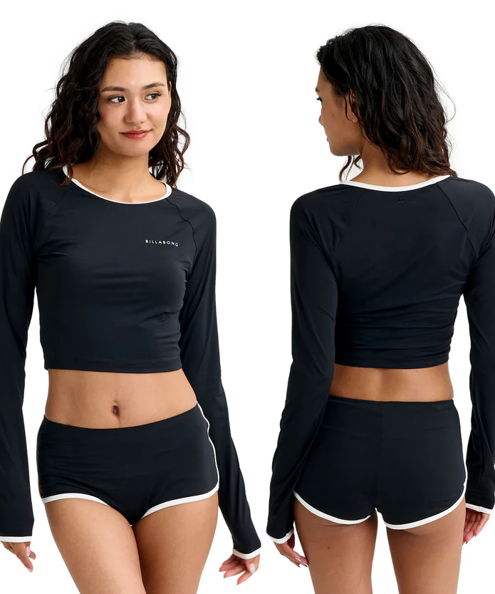 Front and back views of a woman wearing a black long-sleeve cropped top and matching black shorts with white trim; Billabong logo on the chest.