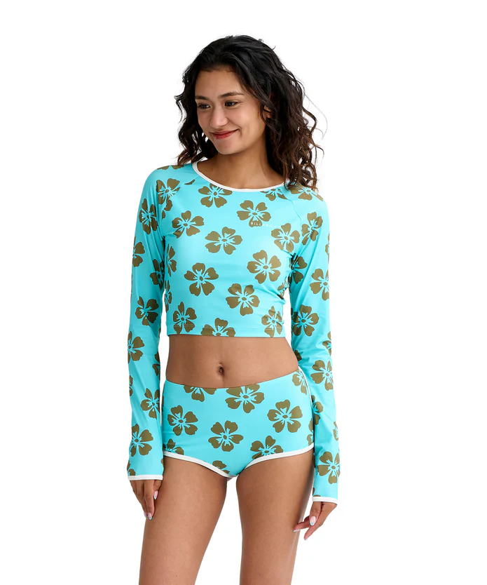 Model wearing a turquoise long-sleeve floral crop top and matching high-waisted shorts with hibiscus print on brown flowers.