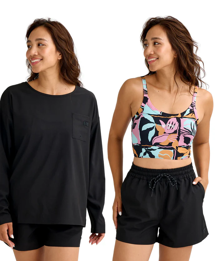 Two women model athletic outfits: left in a black long-sleeve top with black shorts; right in a colorful tropical-print sports bra with black drawstring shorts.