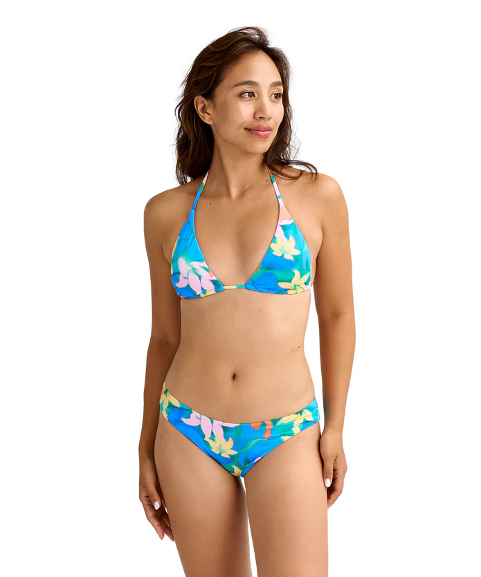 Woman wearing a blue floral bikini, standing and looking to the side, with a tropical print.