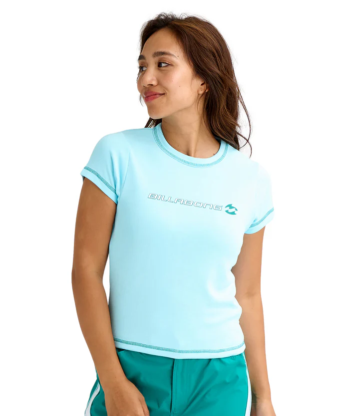 Woman wearing a light blue Billabong T‑shirt and teal shorts, looking to her left in a casual athletic pose.