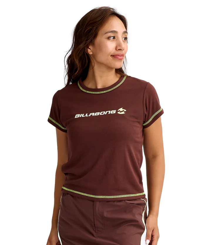 Woman modeling a brown Billabong T-shirt with lime-green trim and matching shorts; logo on the chest, facing to the right.
