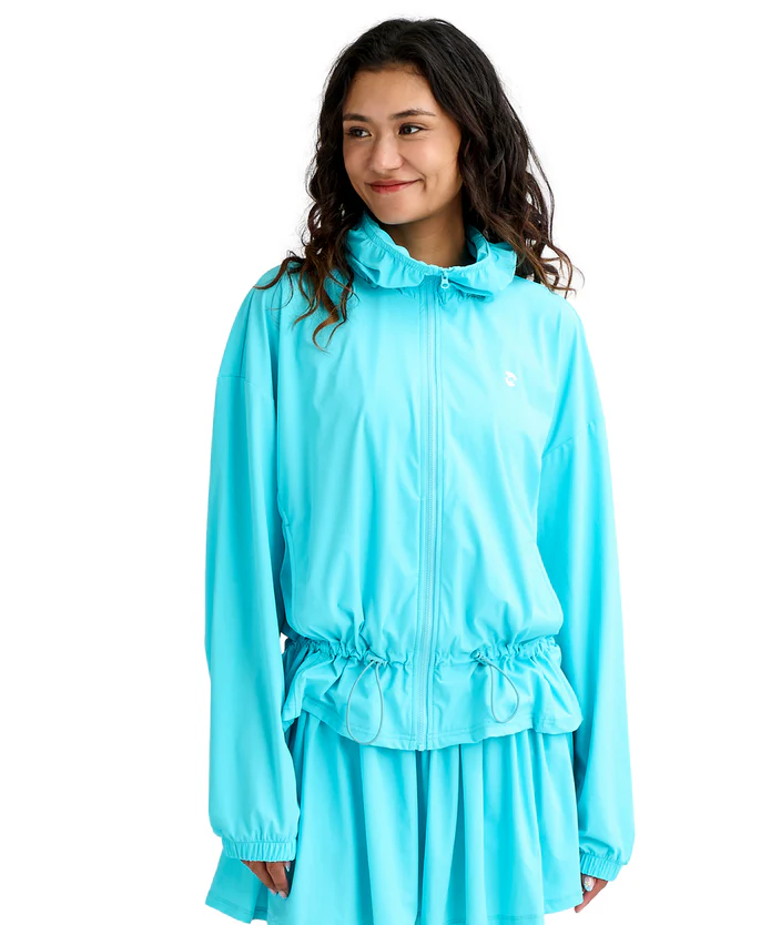 Woman wearing a bright turquoise windbreaker with a drawstring waist and hood, smiling against a white background.
