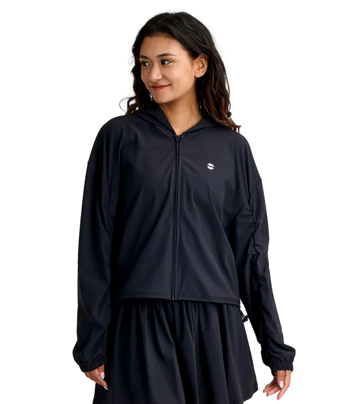Woman wearing a navy windbreaker with hood and zip-front, small white logo on left chest.