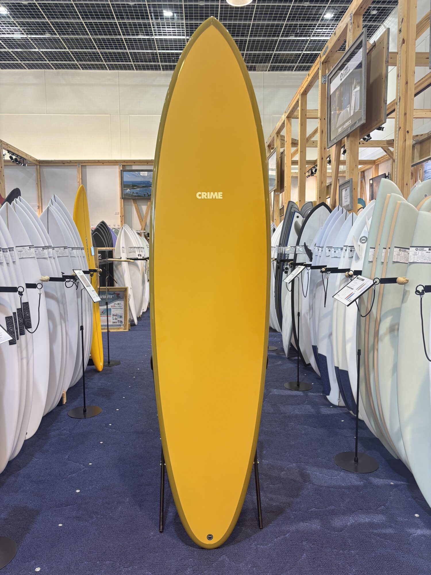 IMG_4168 - SHOP NEWS | ムラサキスポーツオンラインストア 通販 Bright yellow surfboard standing upright in the center of a surf shop display with many white and light-colored boards around it in racks.