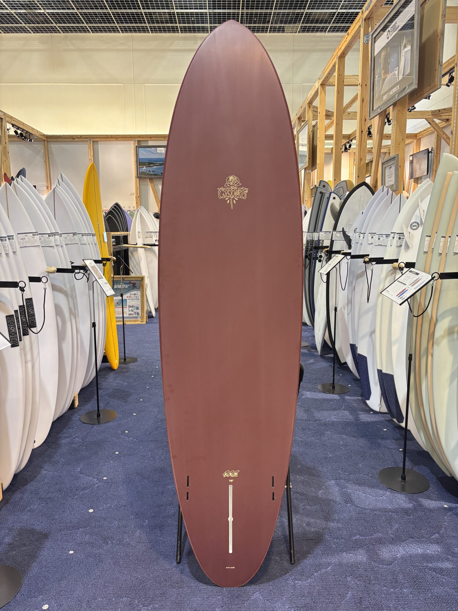 Tall maroon surfboard on display in a shop, surrounded by white and colored boards in a showroom.