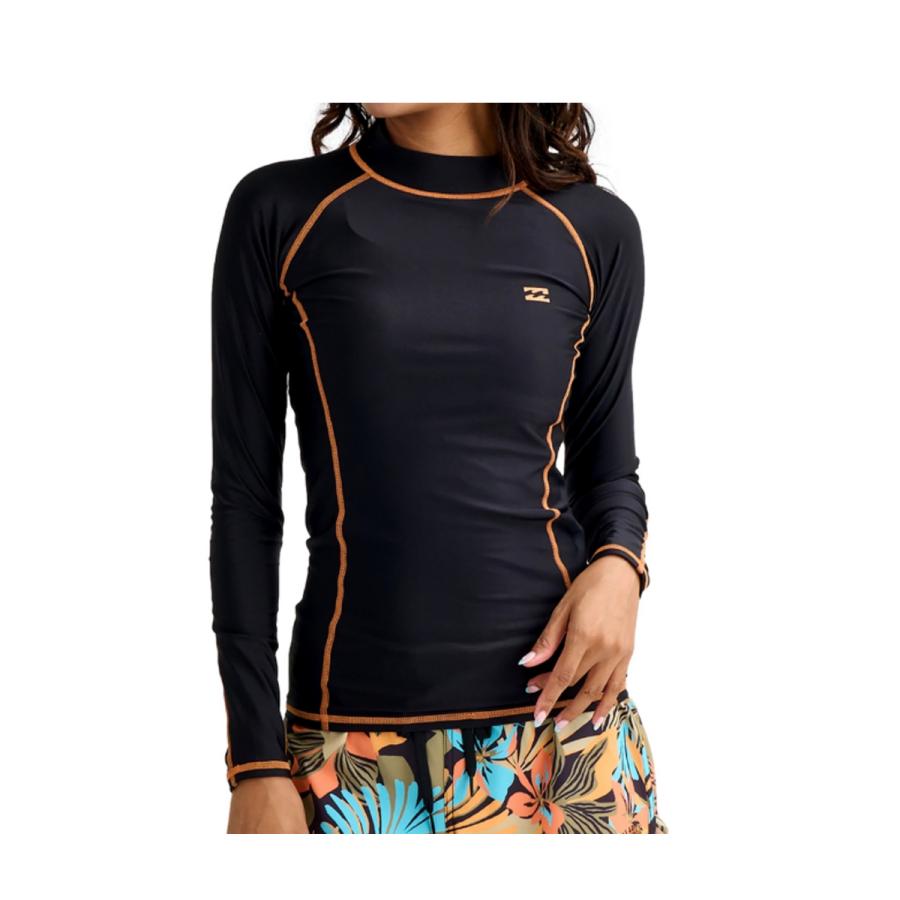 Woman wearing a black long-sleeve rash guard with orange contrast stitching and tropical-print shorts.