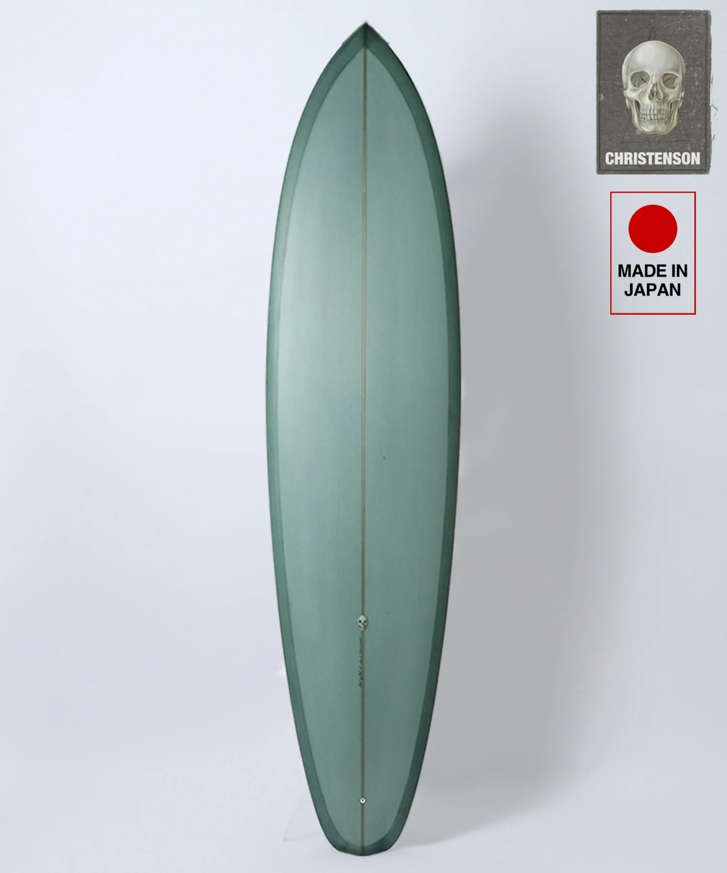 Teal surfboard standing upright against a white backdrop, with two labels on the upper right: a skull image and 'Made in Japan' text.