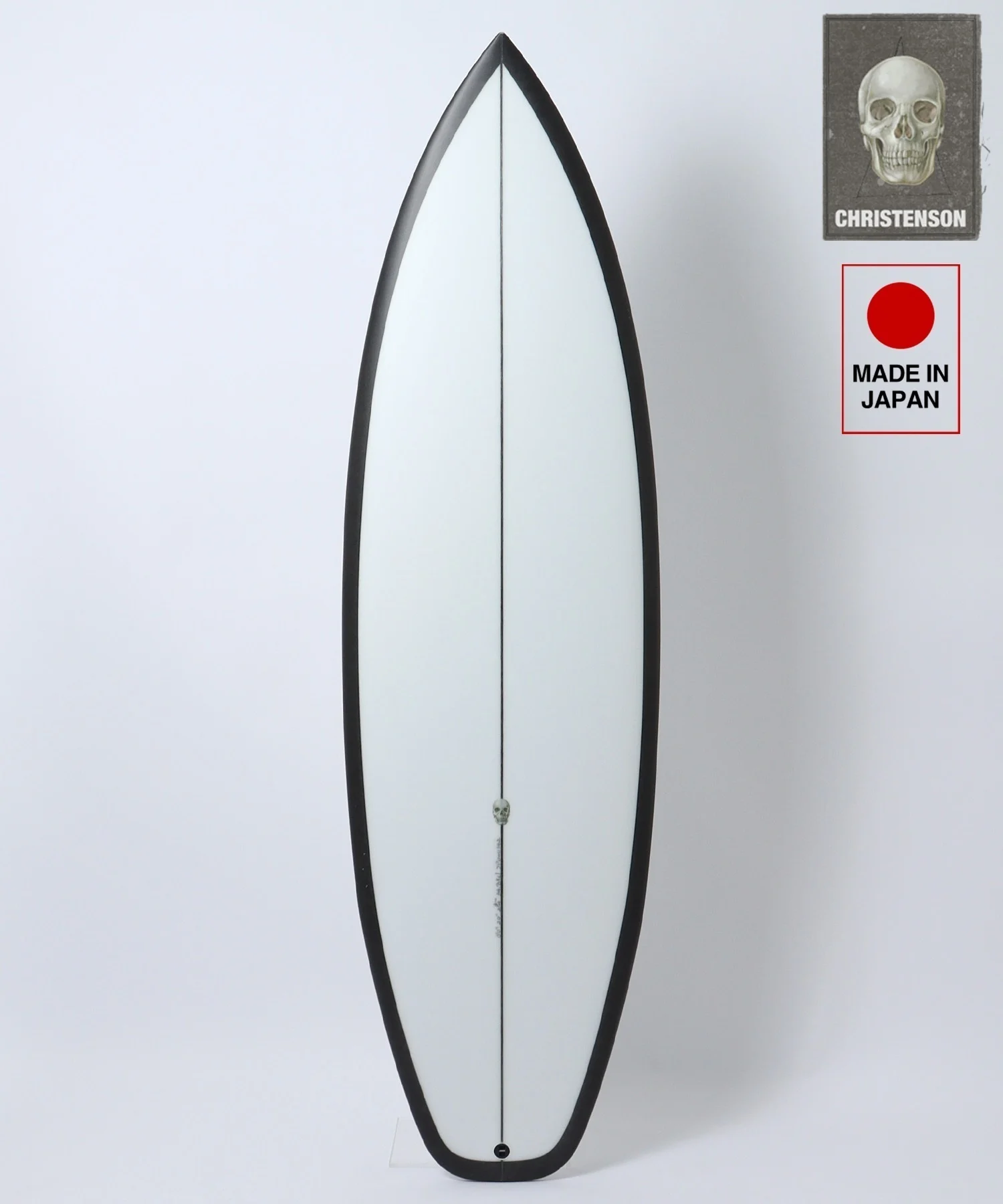 White surfboard with a black edge and center seam, photographed against a light background; brand stickers in the top-right corner (skull image and 'Made in Japan').