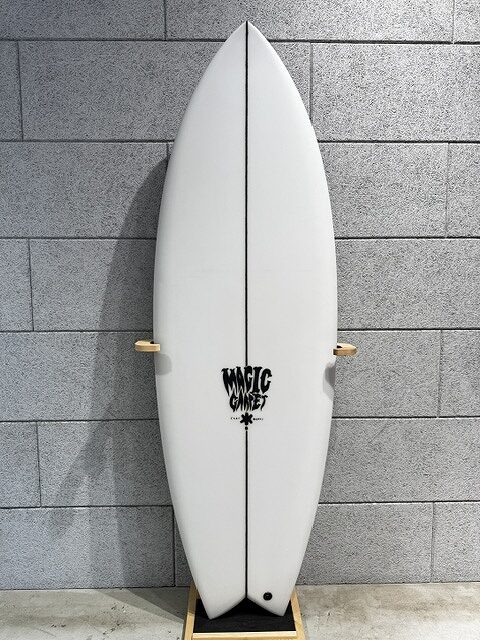 White surfboard with a black center seam, mounted on a wooden stand against a gray brick wall; logo near center.