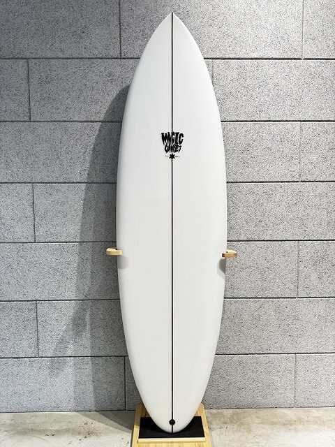 White surfboard standing upright against a gray brick wall on a wooden rack, featuring a black center stringer and a logo near the top.