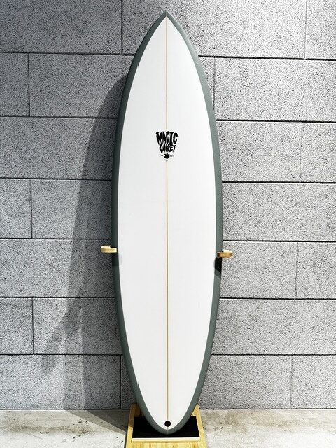 White surfboard with a dark green edge mounted vertically on a wooden display stand against a gray brick wall.