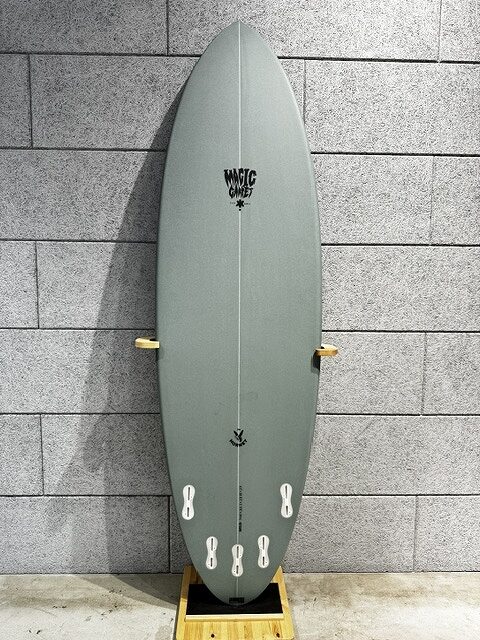 Gray-green surfboard standing upright on a wooden display stand against a gray brick wall.