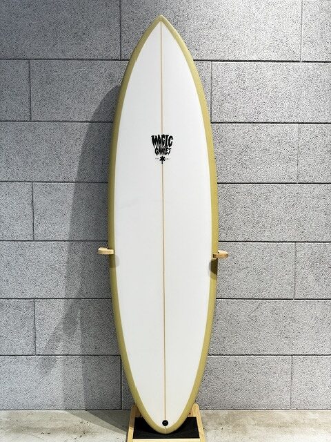 White surfboard with yellow rails stands upright on a wooden rack against a gray brick wall.