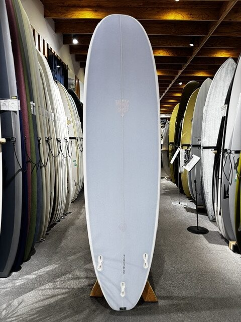 Light blue surfboard standing upright on a wooden stand in a surf shop, surrounded by other boards on racks.