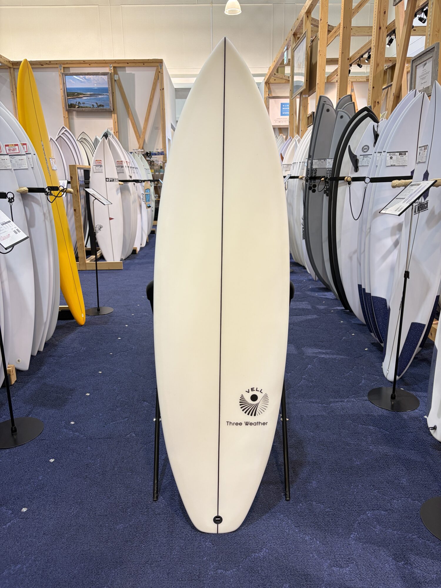 IMG_6165 - SHOP NEWS | ムラサキスポーツオンラインストア 通販 Center white surfboard with 'Three Weather' logo standing upright in a surf shop, surrounded by racks of boards on all sides.