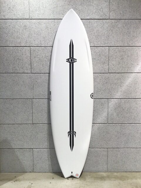 s-image2 - SHOP NEWS | ムラサキスポーツオンラインストア 通販 White surfboard with a black double stripe and small logos, standing upright against a gray tiled wall.