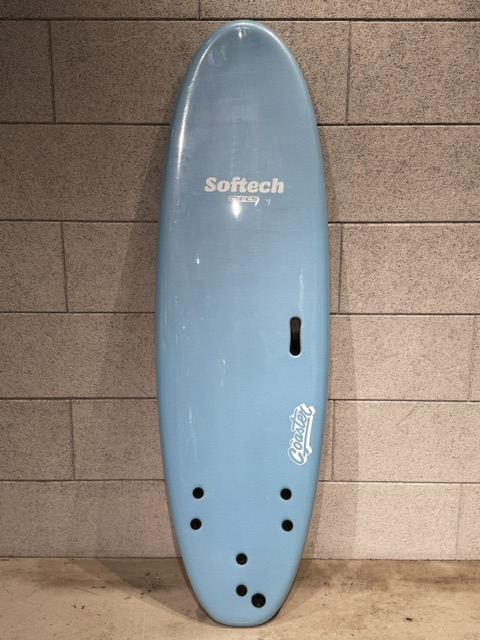 Light blue Softech bodyboard leaning against a gray brick wall.