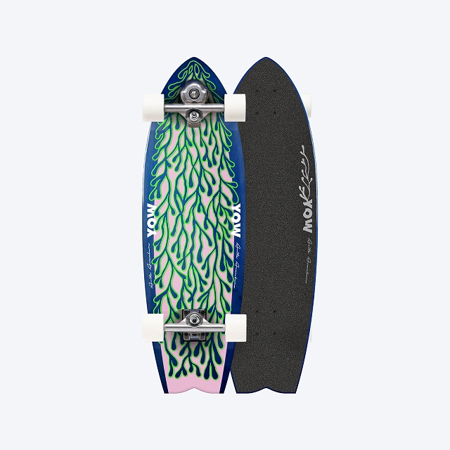 Two longboards standing upright side by side: left deck features a blue surface with a green coral-like pattern and white wheels; right deck has a black grip-tape surface with a white signature logo.