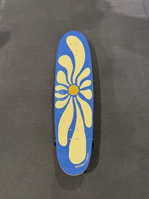 Blue skateboard deck featuring a large yellow flower on a blue background, on a gray surface.