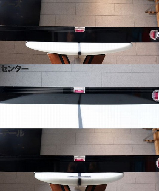White surfboard resting on display racks, photographed from above, with black supports and pink end caps in a showroom setting.