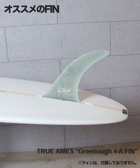 Surfboard with a translucent green fin attached, lying on a light tiled wall; text says 'オススメのFIN' at top and 'TRUE AMES "Greenough 4-A FIN"' along the bottom. Fin is not included as noted in small print.